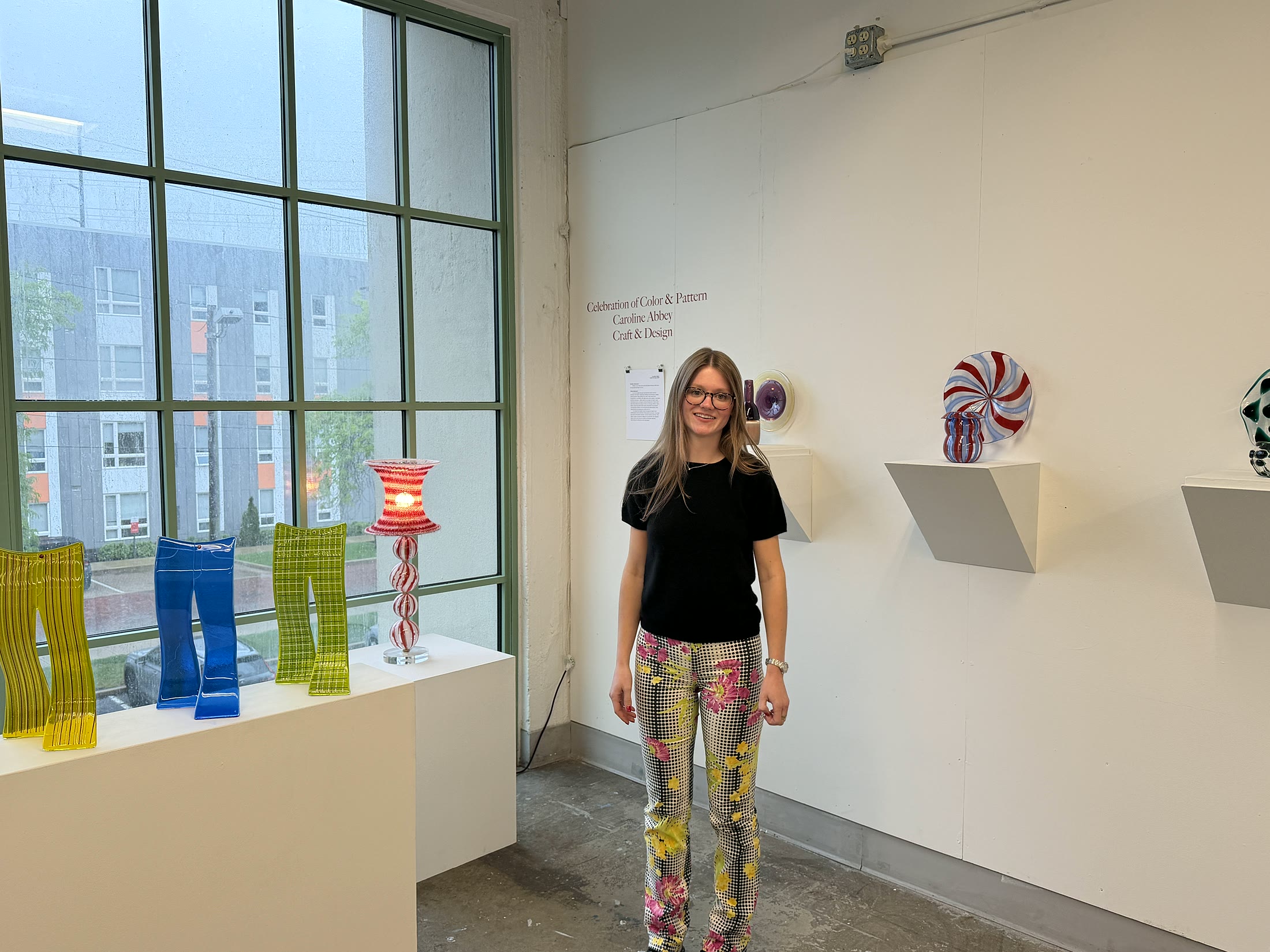 Caroline Abbey beside her glass work in a gallery